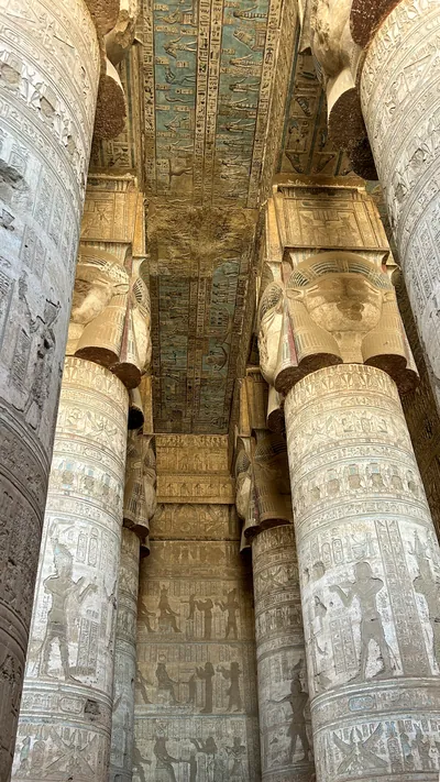 Ancient hieroglyphs and carved columns with painted ceiling details inside Dendera Temple in Egypt.