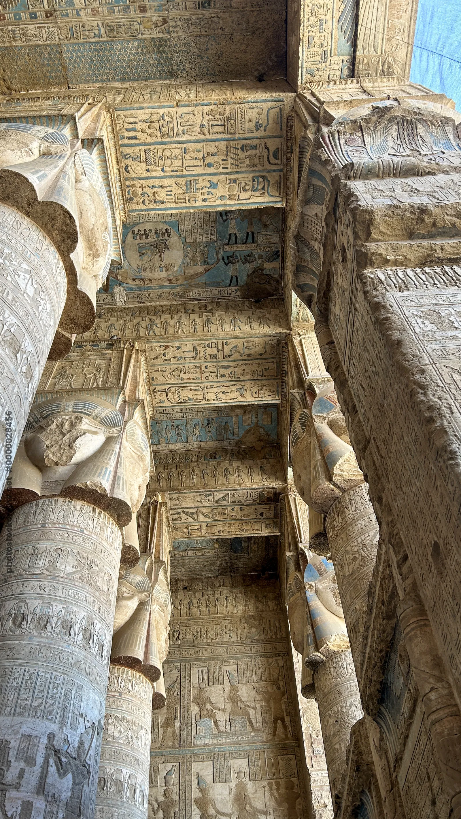 Ancient hieroglyphs and carved columns with painted ceiling details inside Dendera Temple in Egypt.