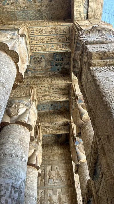 Ancient hieroglyphs and carved columns with painted ceiling details inside Dendera Temple in Egypt.