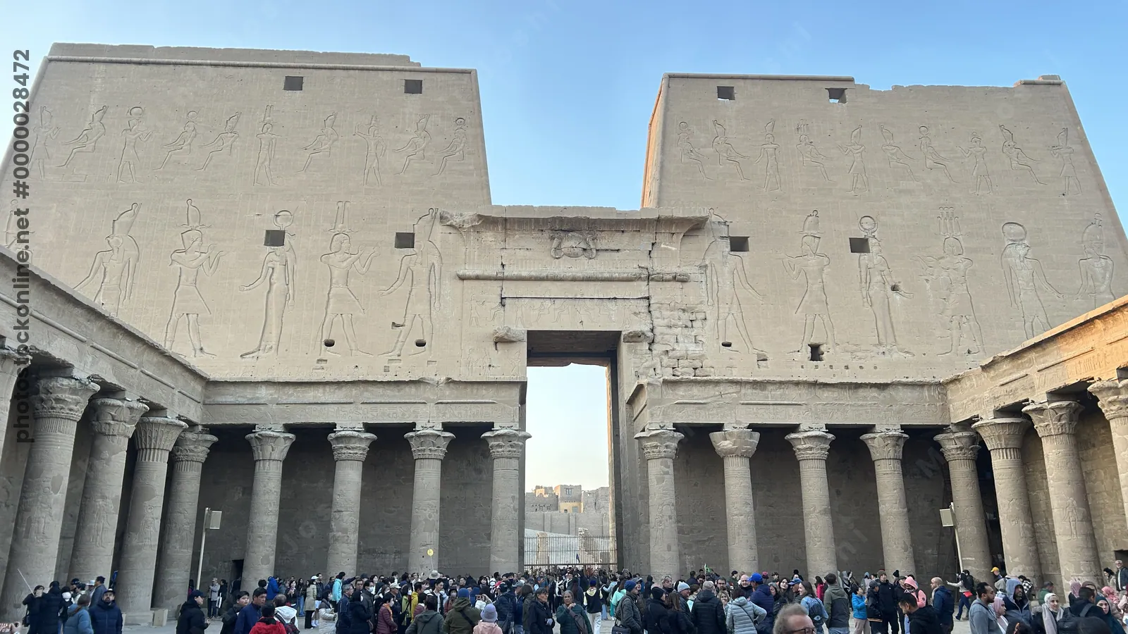 Edfu, Egypt - Feb 9, 2025: Tourists gathered in the forecourt before the monumental entrance pylons of the Temple of Edfu in Egypt, decorated with anc