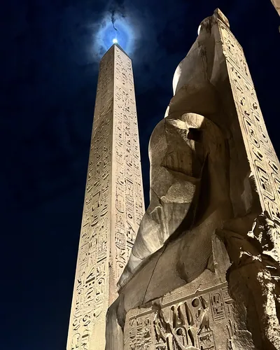 Luxor, Egypt - Feb 9, 2025: Low-angle night view of the illuminated obelisk and colossal statue of Pharaoh Ramses II at Luxor Temple in Egypt, with th