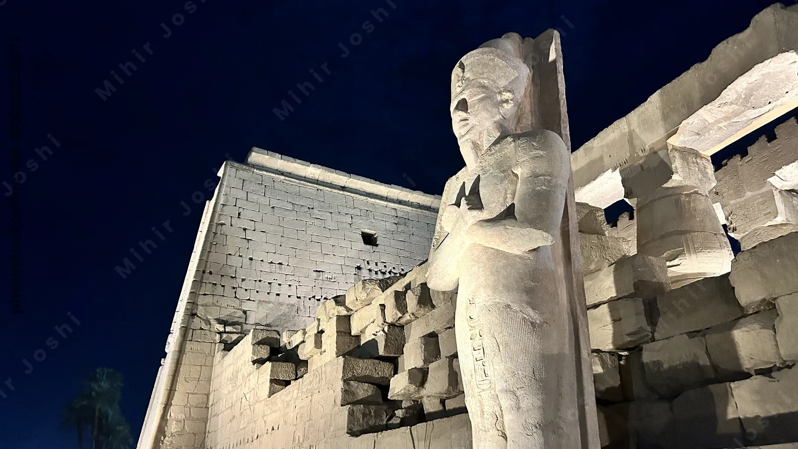Luxor, Egypt - Feb 9, 2025: Night view of the illuminated colossal standing statue of Pharaoh Ramses II at the entrance of Luxor Temple in Egypt.