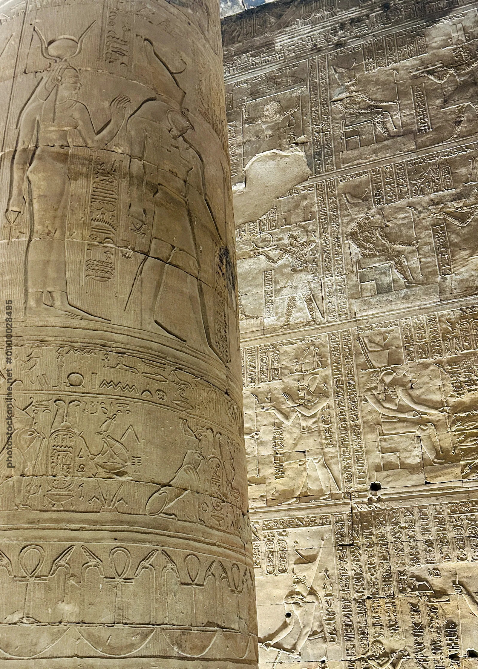 Edfu, Egypt - Feb 9, 2025: Detailed view of a carved column and wall reliefs with hieroglyphs and depictions of ancient deities at the Temple of Horus
