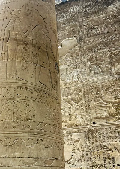 Edfu, Egypt - Feb 9, 2025: Detailed view of a carved column and wall reliefs with hieroglyphs and depictions of ancient deities at the Temple of Horus