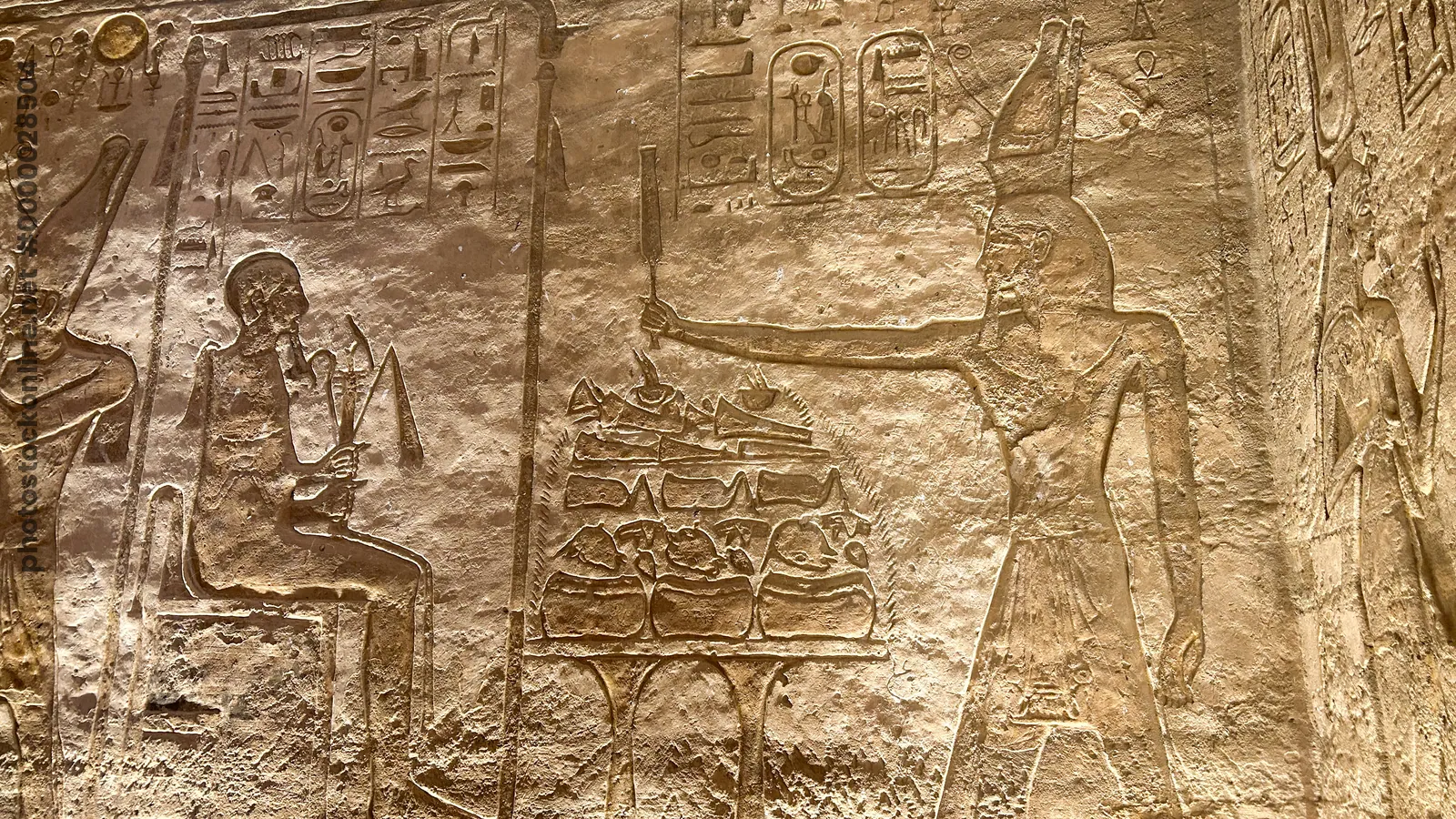 Aswan, Egypt - Feb 8, 2025: Ancient relief at Abu Simbel showing Pharaoh making offerings to the creator god Ptah, seated with hieroglyphs behind.