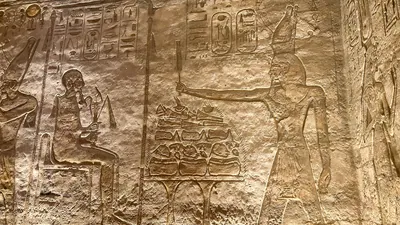 Aswan, Egypt - Feb 8, 2025: Ancient relief at Abu Simbel showing Pharaoh making offerings to the creator god Ptah, seated with hieroglyphs behind.