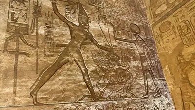 Aswan, Egypt - Feb 8, 2025: Ancient wall relief at Abu Simbel showing Pharaoh smiting enemies before the sun god Ra.