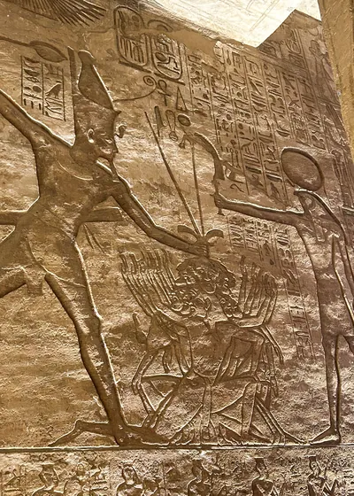Aswan, Egypt - Feb 8, 2025: Ancient wall relief at Abu Simbel showing Pharaoh smiting enemies before the sun god Ra.