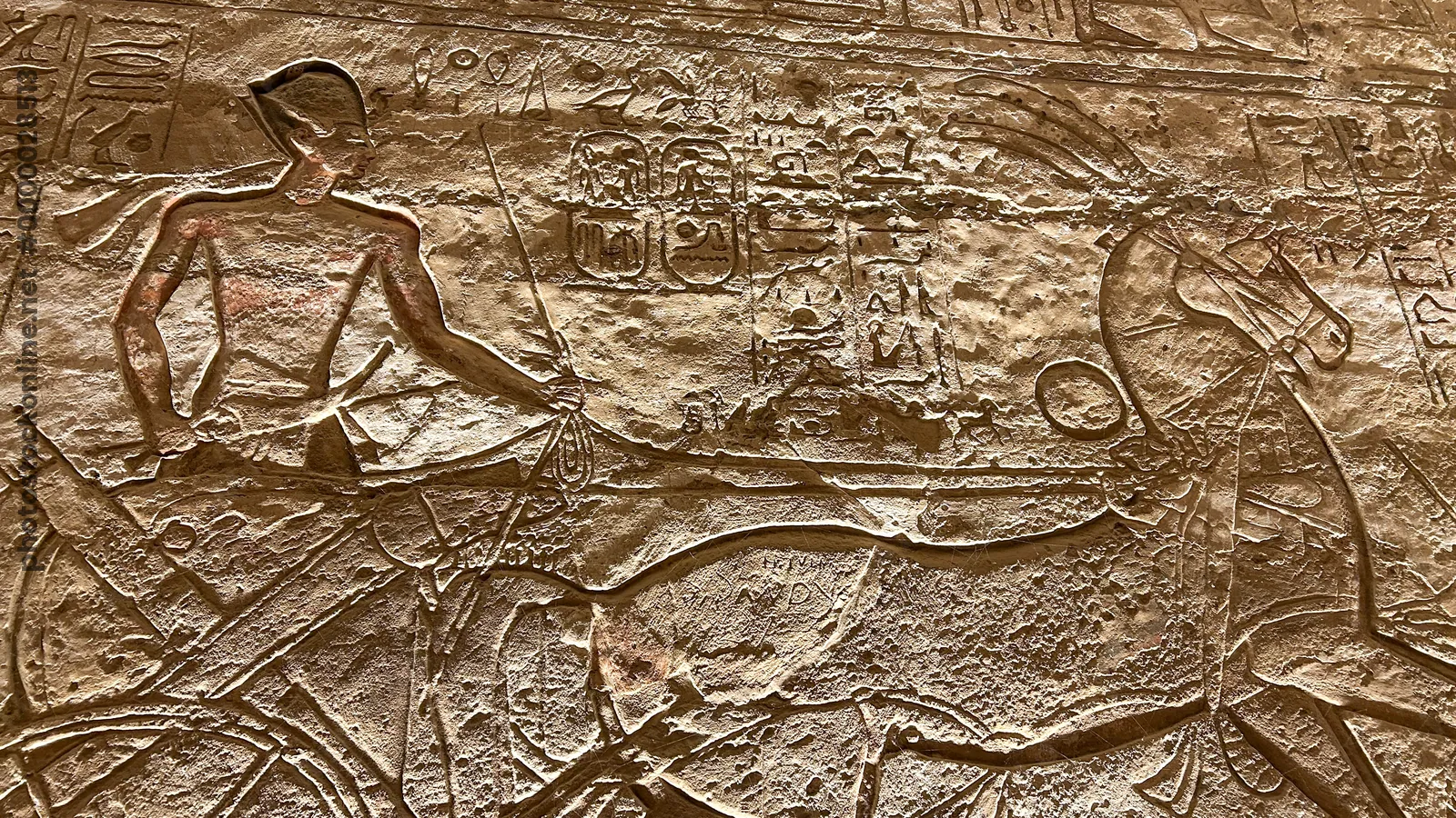 Aswan, Egypt - Feb 8, 2025: Ancient relief at Abu Simbel showing Pharaoh in a chariot with bow and hieroglyphs.