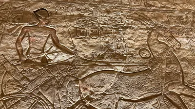Aswan, Egypt - Feb 8, 2025: Ancient relief at Abu Simbel showing Pharaoh in a chariot with bow and hieroglyphs.
