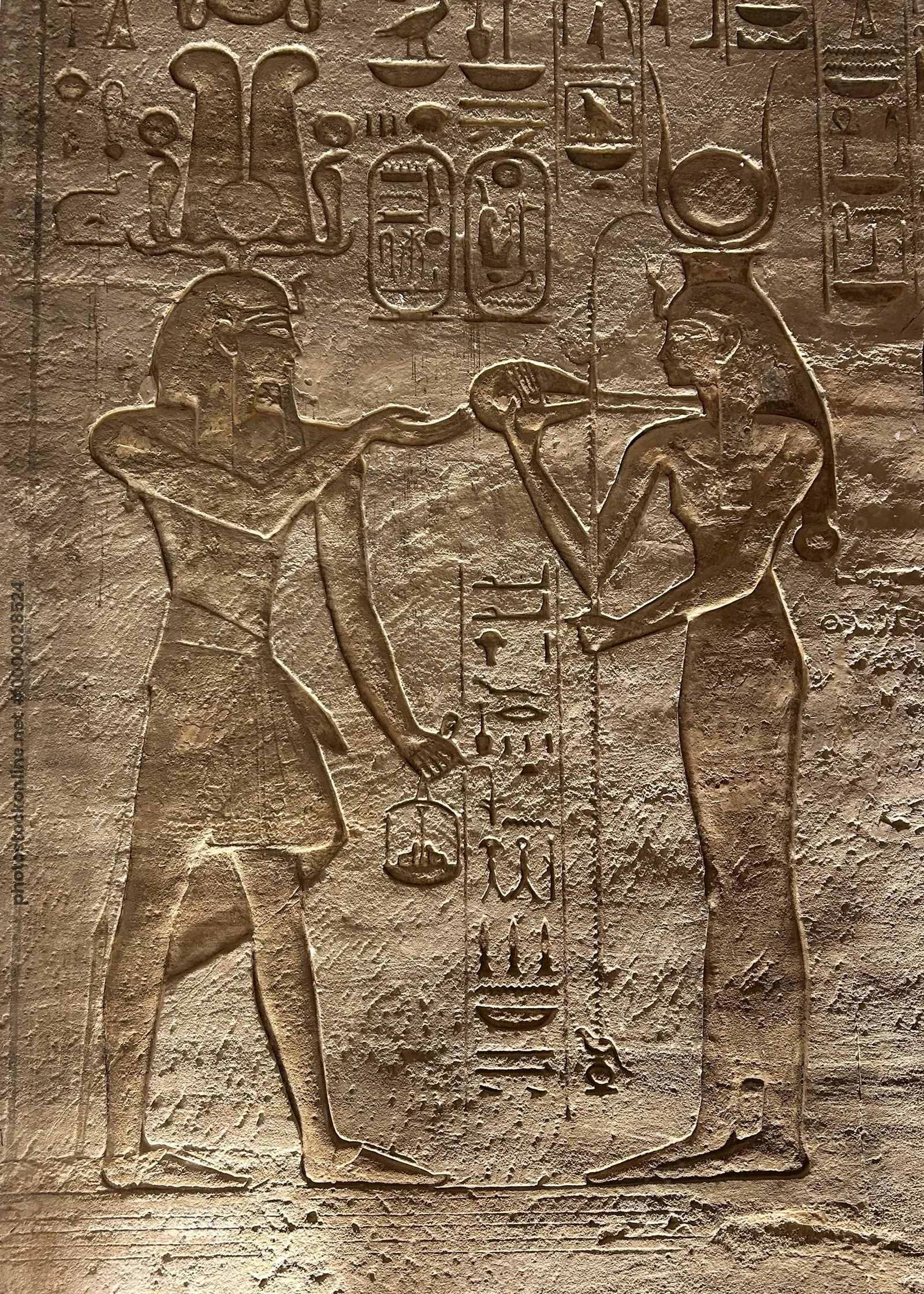 Detailed rock-cut relief at Abu Simbel, Egypt, depicting a pharaoh presenting offerings to goddess Hathor, with hieroglyphs and intricate carvings.
