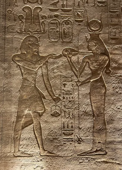 Detailed rock-cut relief at Abu Simbel, Egypt, depicting a pharaoh presenting offerings to goddess Hathor, with hieroglyphs and intricate carvings.