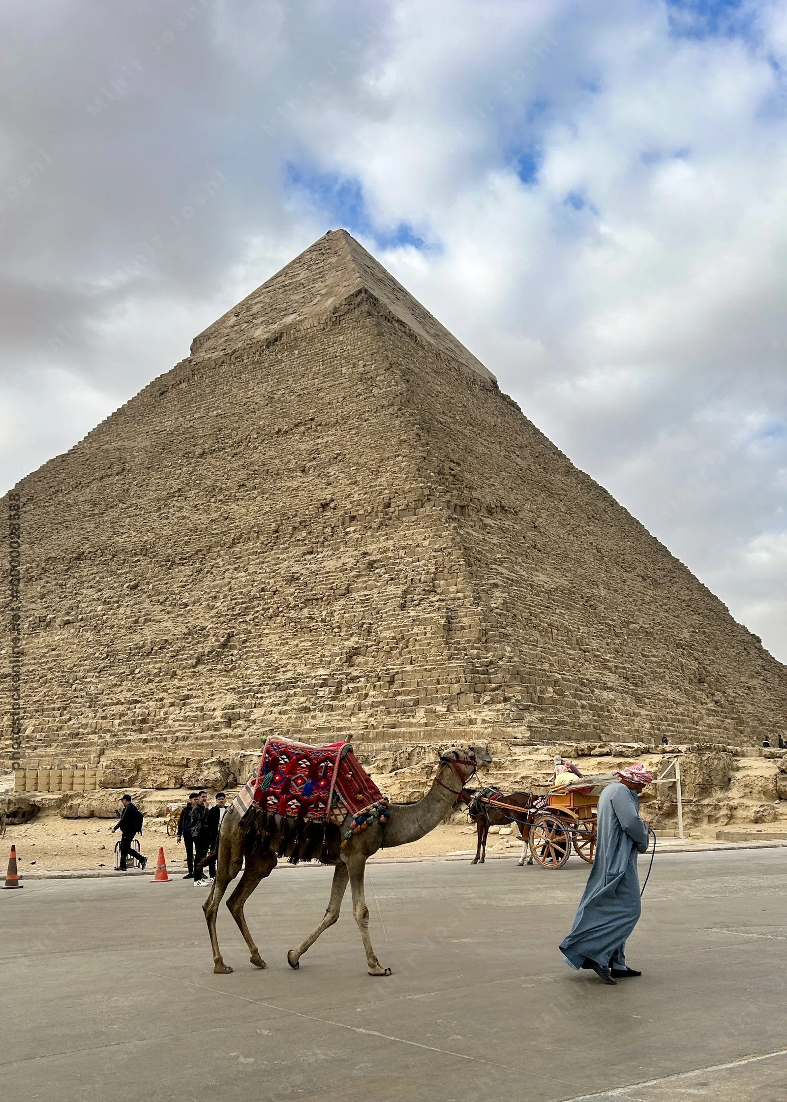 A Bedouin man offers a camel ride to tourists near the Great Pyramid of Giza, a famous archaeological site in Egypt.