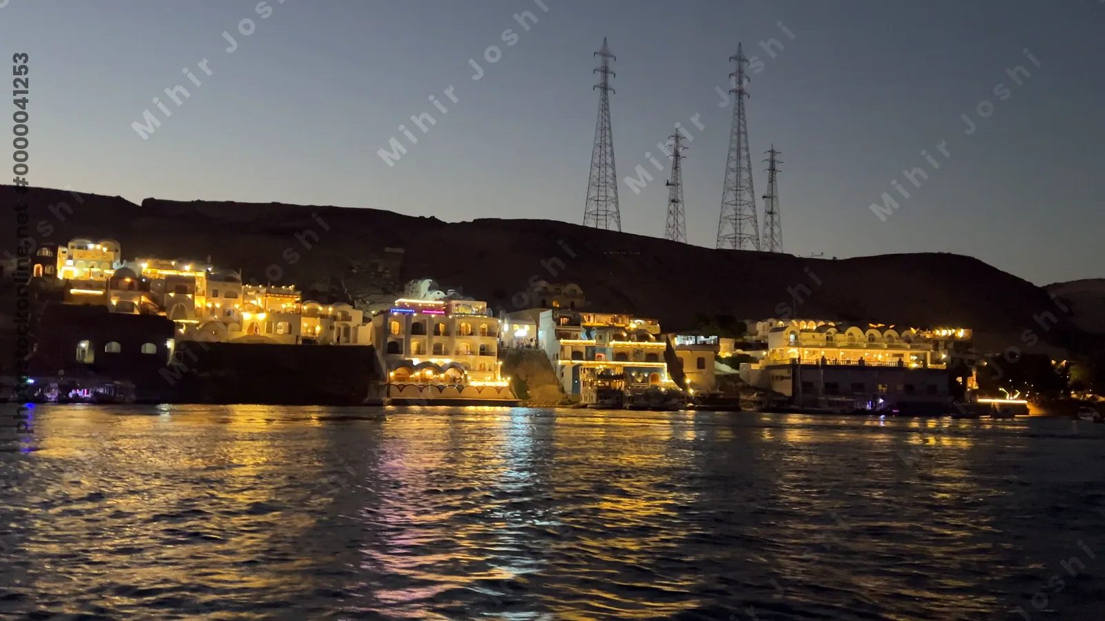 Scenic boat ride on the Nile River at dusk with a Nubian village illuminated by lights along the riverbank in Aswan, Egypt.