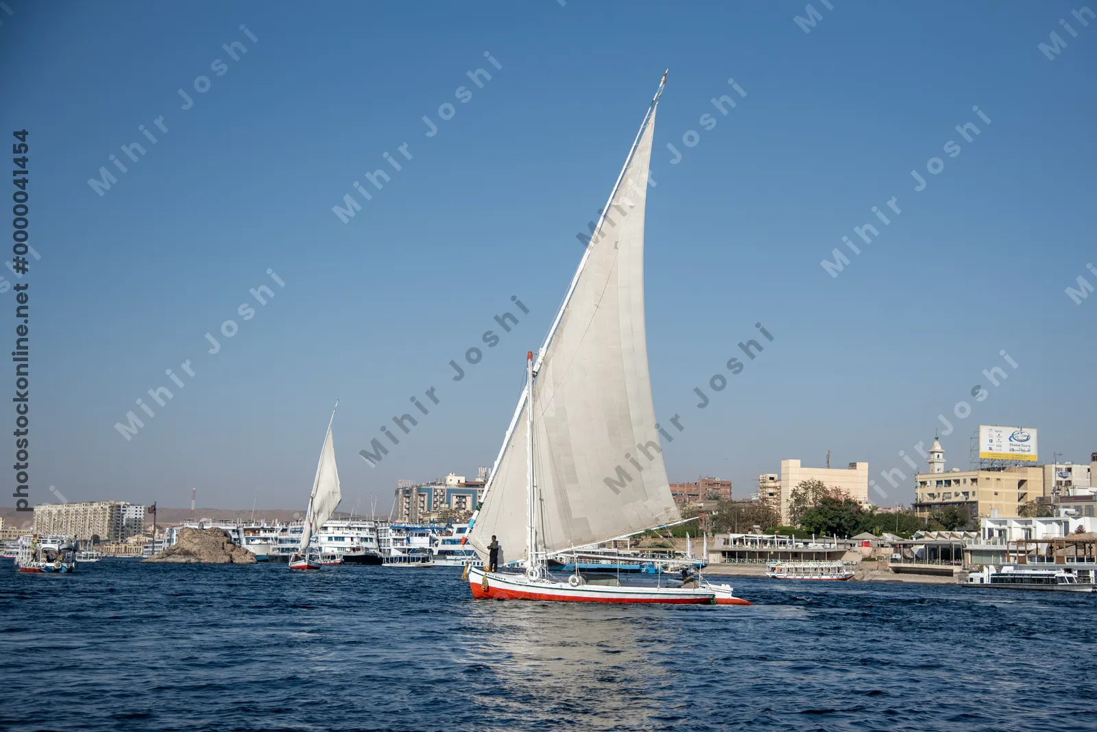 Aswan, Egypt - Feb 7, 2025:  A traditional felucca sails the clear, blue waters of the Nile River near Aswan, Egypt