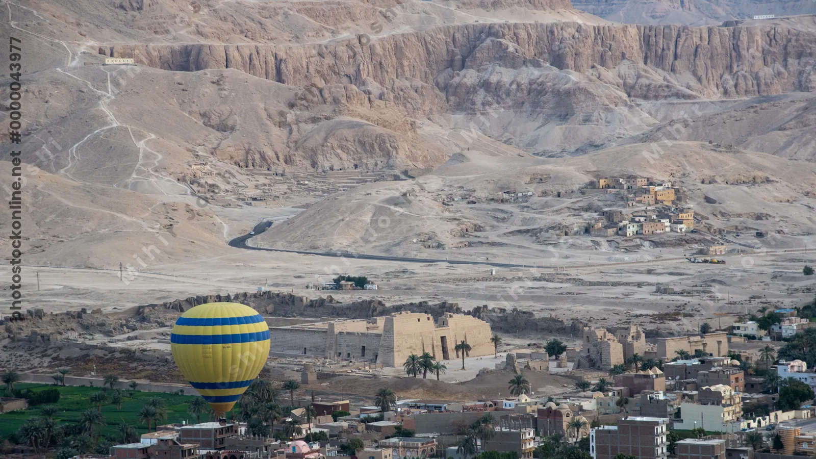 Luxor, Egypt - Feb 10, 2025: Hot air balloon floats above Luxor, Egypt, with scenic view of Medinet Habu Temple, mountains, and desert landscape at sunrise