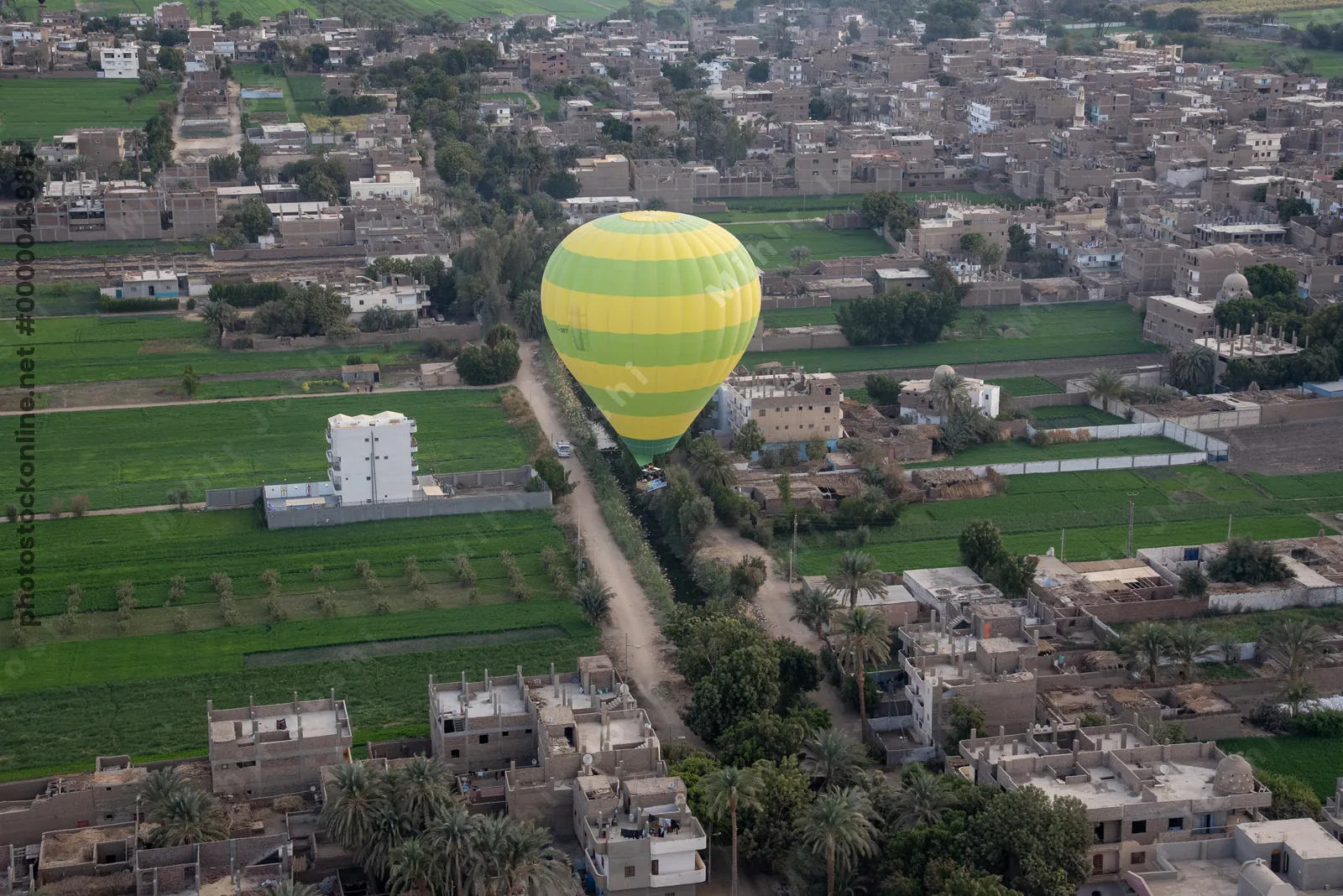 Hot air balloon hovers above lush farmland and traditional houses near Luxor, Egypt, during sunrise
