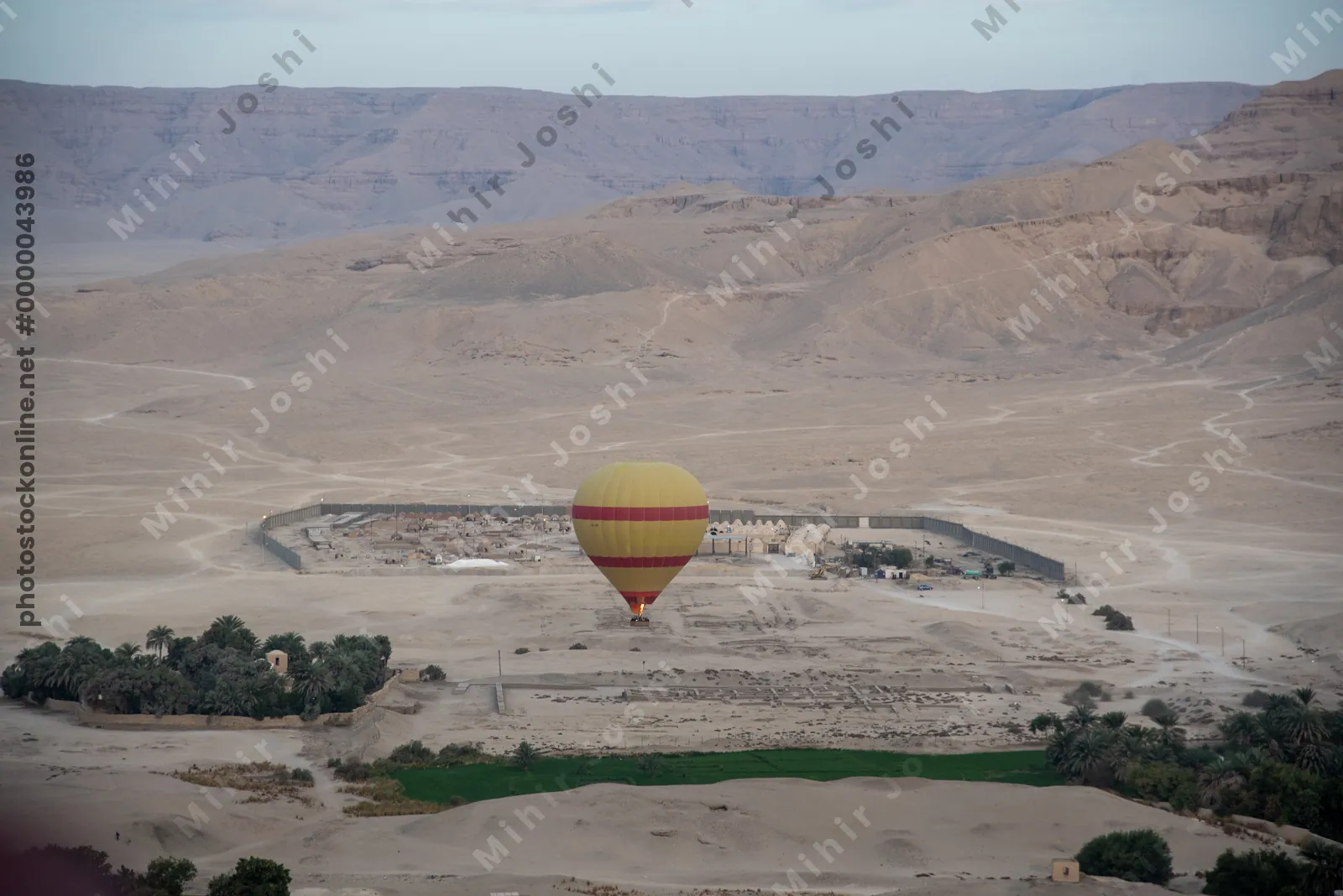 Hot air balloon descends near a desert village and green oasis in Luxor, Egypt.