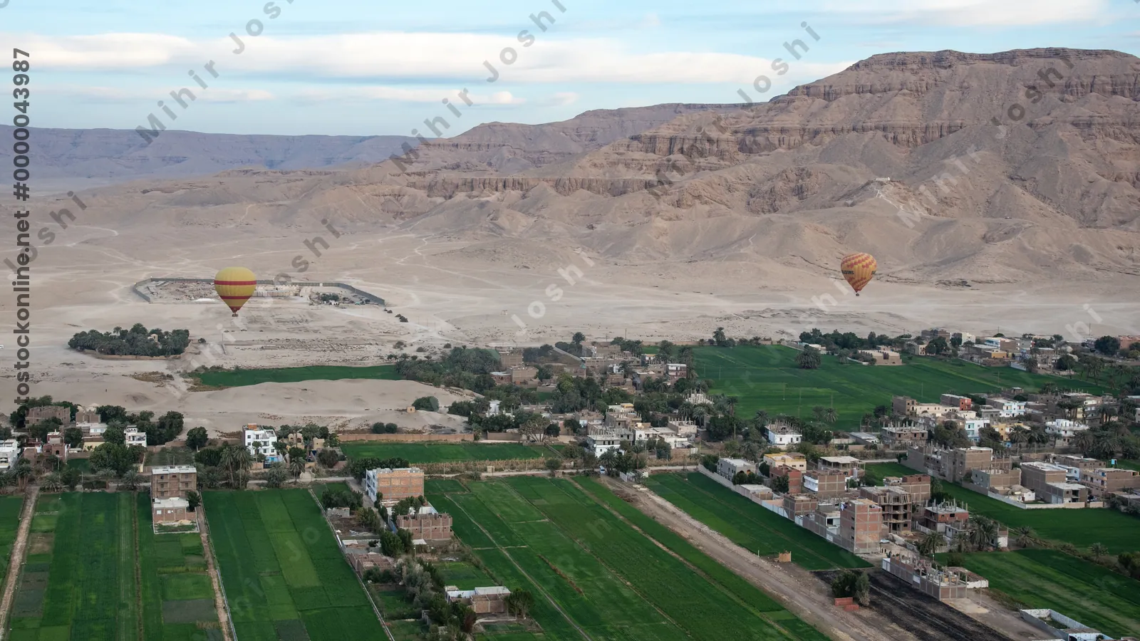 Luxor, Egypt - Feb 10, 2024: Hot air balloons float over the desert near Luxor, Egypt. Mountains and green farm fields complete this dramatic sunrise scene.