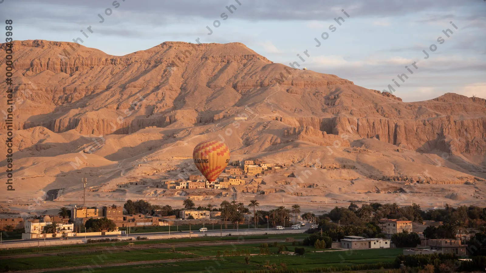 Luxor, Egypt - Feb 10, 2024: Hot air balloon over farms at sunrise in Luxor, Egypt. Distant mountains, hillside houses, and a road cutting through the Nile valley.