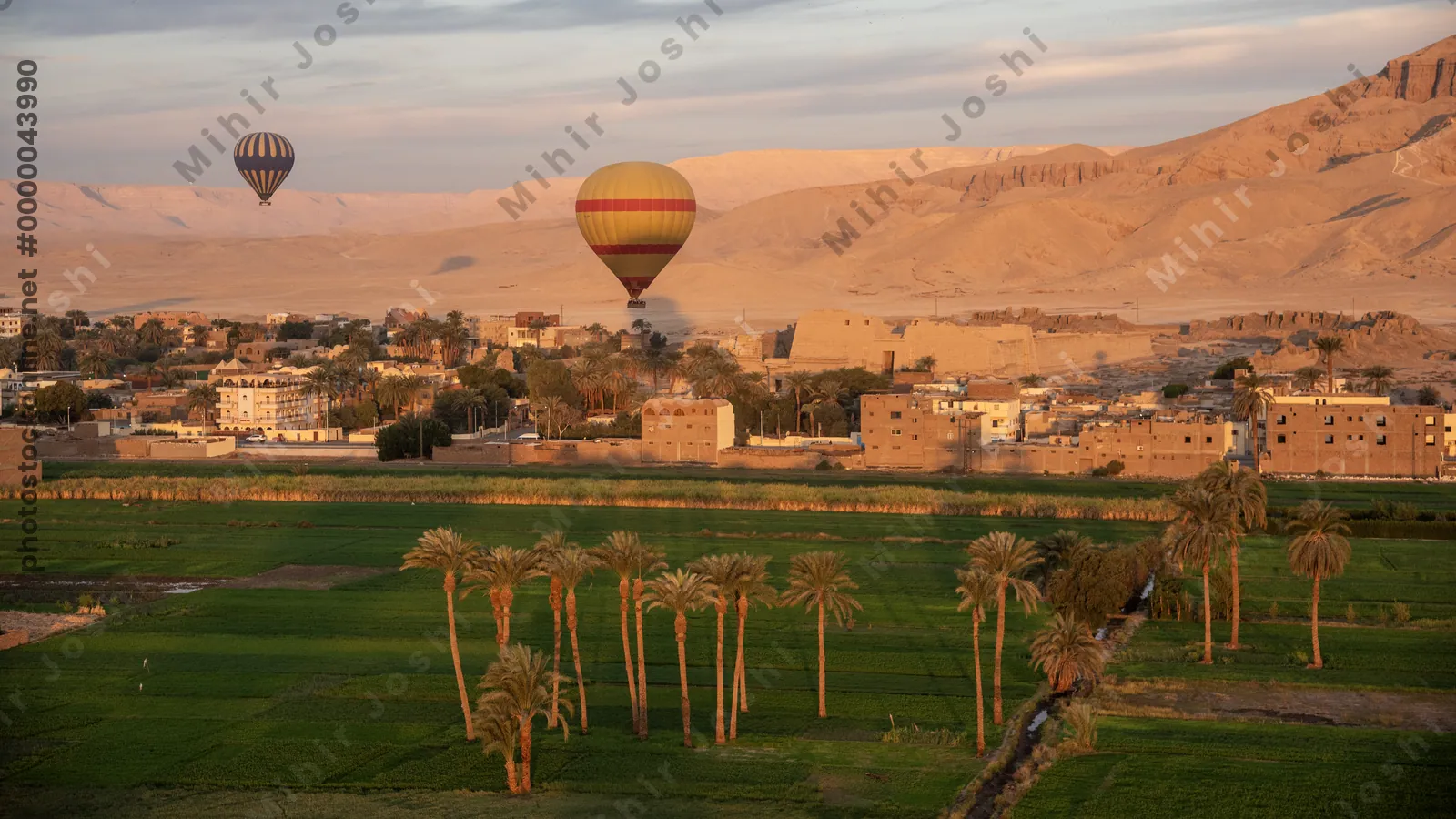 Hot air balloon over farms at sunrise in Luxor, Egypt. Distant mountains, hillside houses, and a road cutting through the Nile valley.