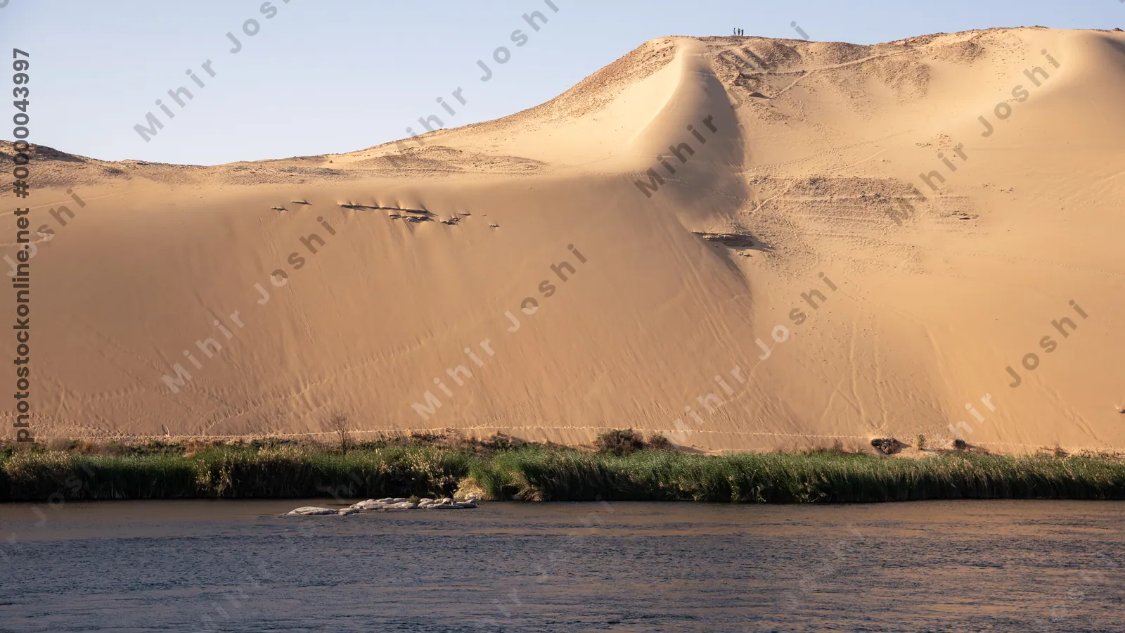 Golden sand dunes lining the Nile River at the First Cataract region near Aswan, Egypt, showcasing a striking desert - river contrast.