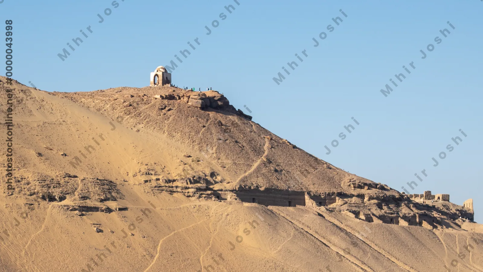 Ancient rock-cut Tombs of the Nobles on the hillside across the Nile River from Aswan, Egypt, seen from the riverbank.