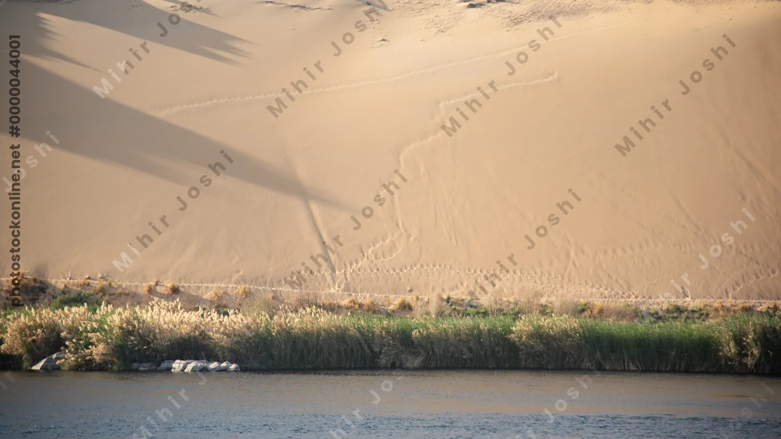 Golden sand dunes lining the Nile River at the First Cataract region near Aswan, Egypt, showcasing a striking desert - river contrast.
