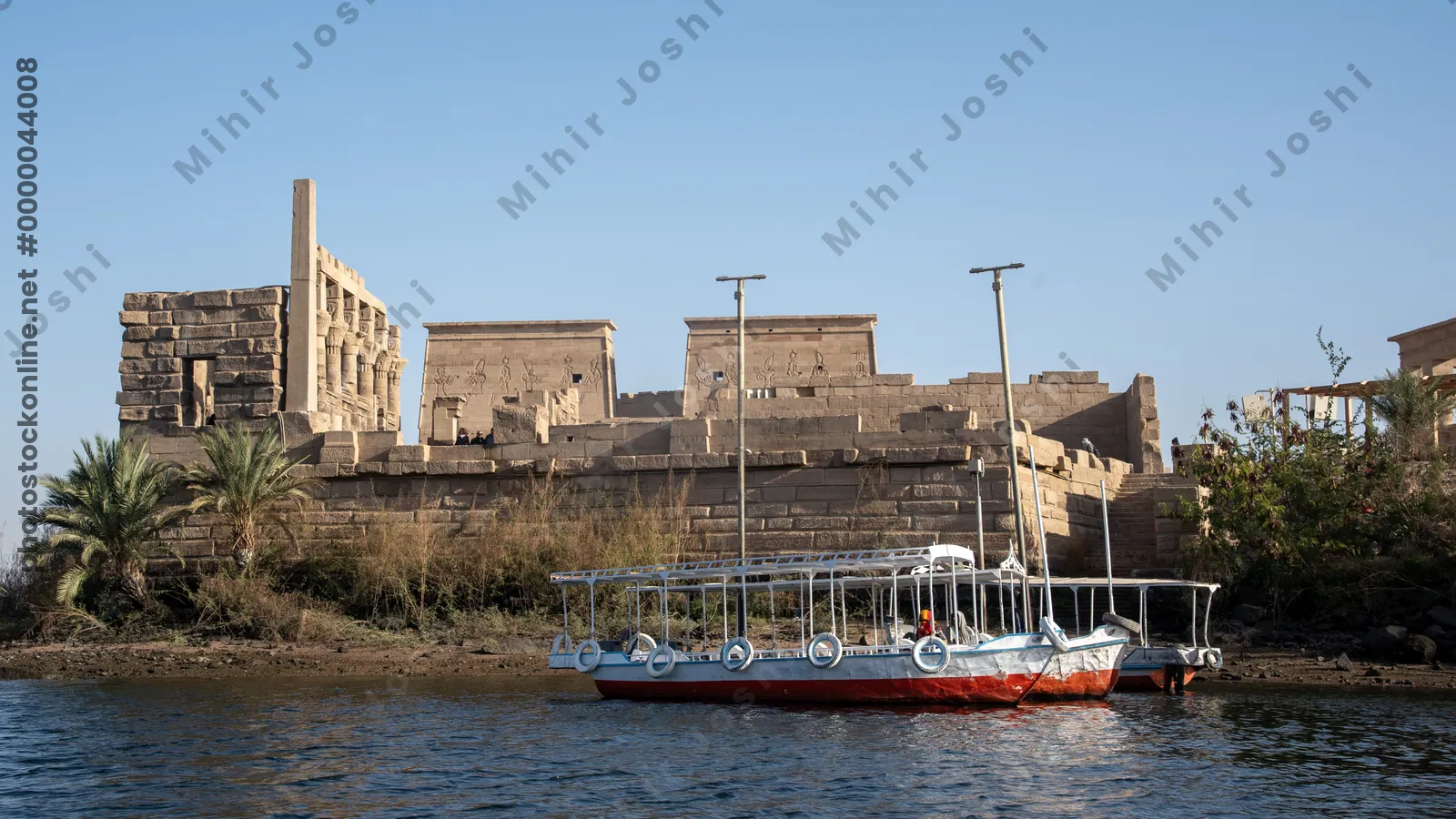 Aswan, Egypt - Feb 7, 2025: Ferry boats docking near the historic Temple of Philae on the Nile River in Aswan, Egypt.