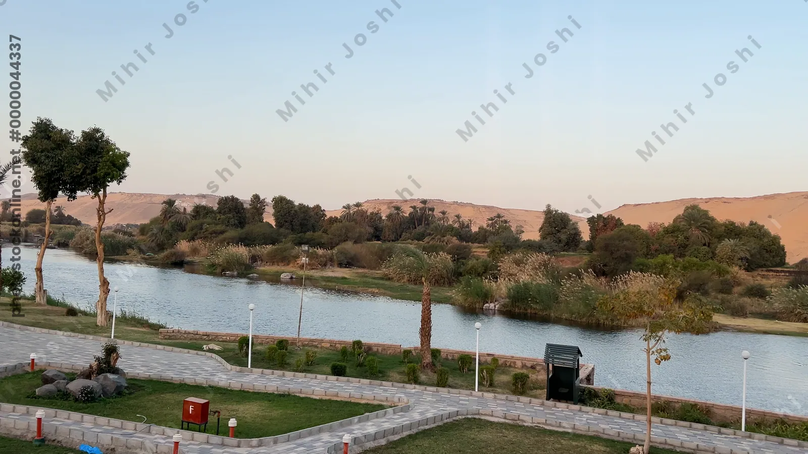 Aswan, Egypt - Feb 7, 2024: Early morning view of the Nile River with lush vegetation and golden sand dunes on the opposite riverbank.
