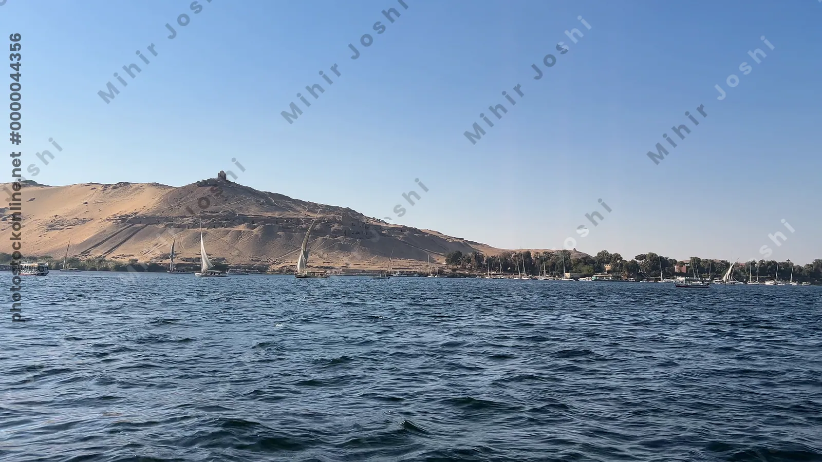 Aswan, Egypt - Feb 7, 2024: Ancient rock-cut Tombs of the Nobles on the hillside across the Nile River from Aswan, Egypt, seen from a boat ride.