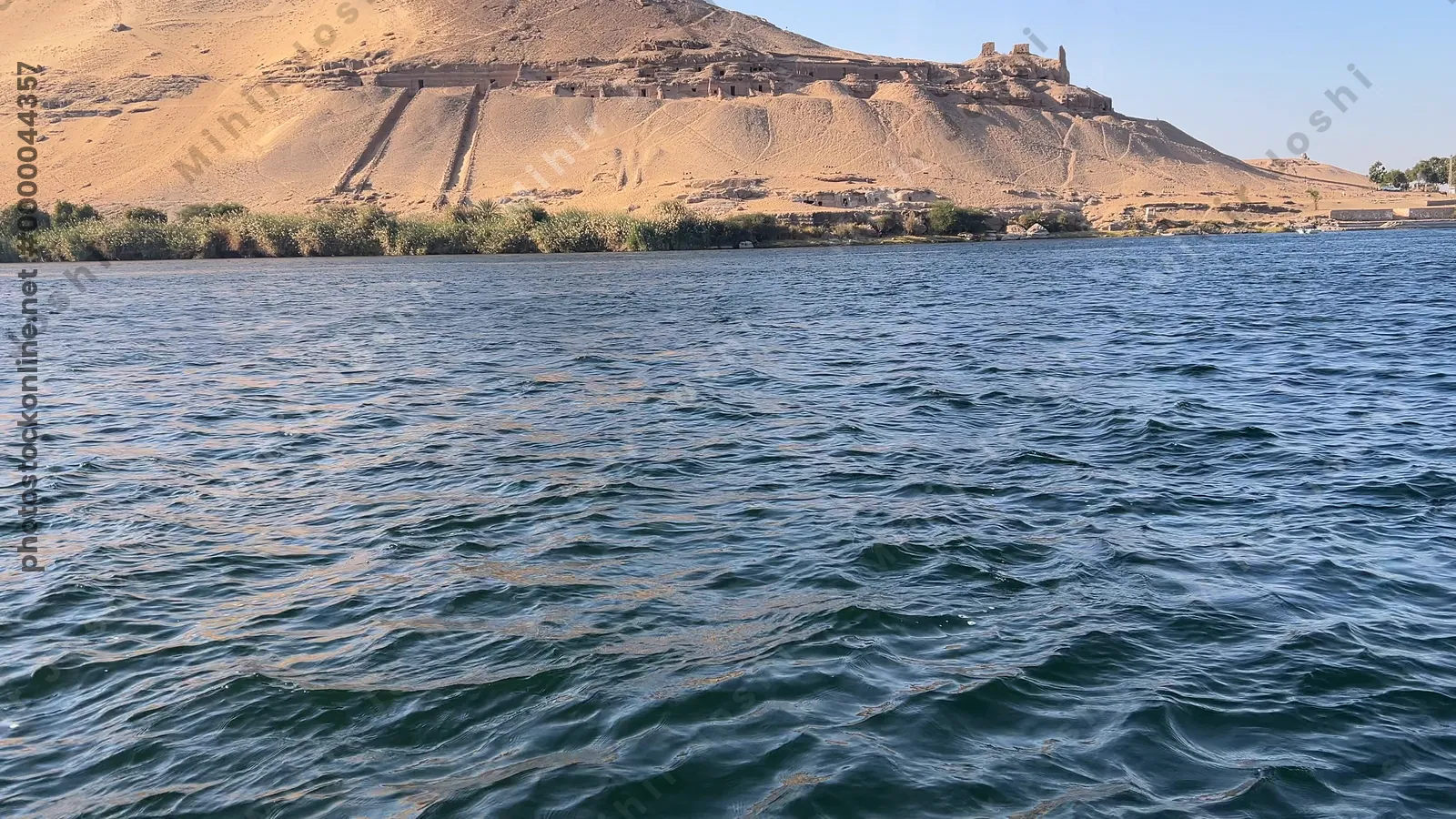 Aswan, Egypt - Feb 7, 2024: Ancient rock-cut Tombs of the Nobles on the hillside across the Nile River from Aswan, Egypt, seen from a boat ride.