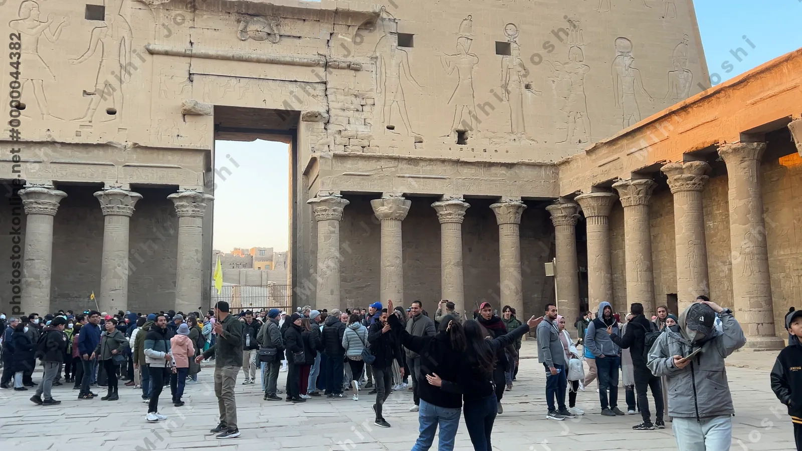 Edfu, Egypt - Feb 9, 2025: Tourists gathered in the forecourt before the monumental entrance pylons of the Temple of Edfu in Egypt, decorated with ancient relief carvings.