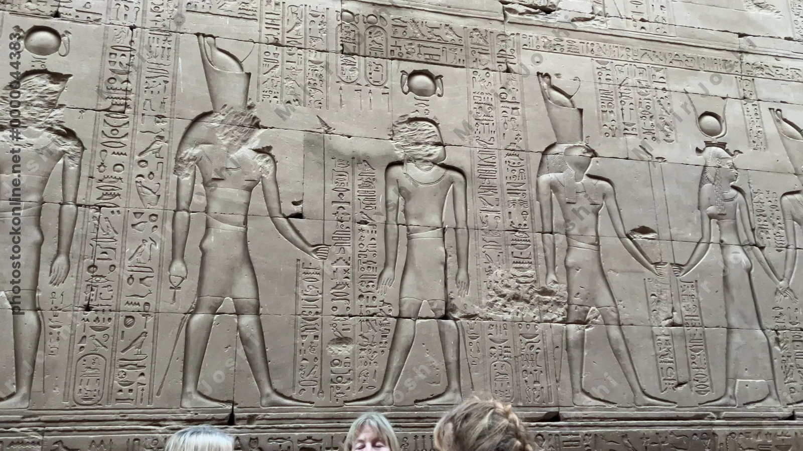 Edfu, Egypt - Feb 9, 2025: A carved sandstone relief at the Temple of Horus in Edfu depicting a procession of gods and the pharaoh, richly inscribed with hieroglyphs.