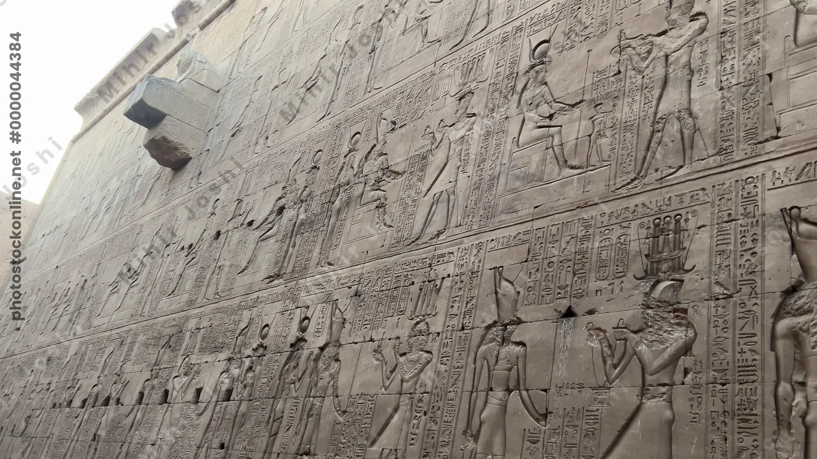 Edfu, Egypt - Feb 9, 2025: Tourists walk between towering sandstone walls richly decorated with relief carvings and hieroglyphs at the Temple of Horus