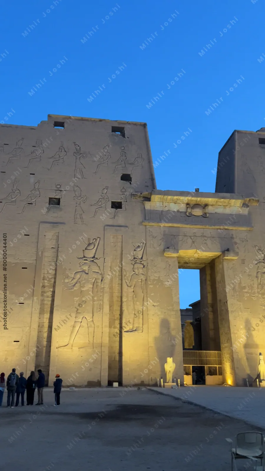 Edfu, Egypt - Feb 9, 2025: View of the illuminated entrance pylon of the Temple of Edfu at dusk in Egypt, decorated with large-scale relief carvings and visited by tourists.
