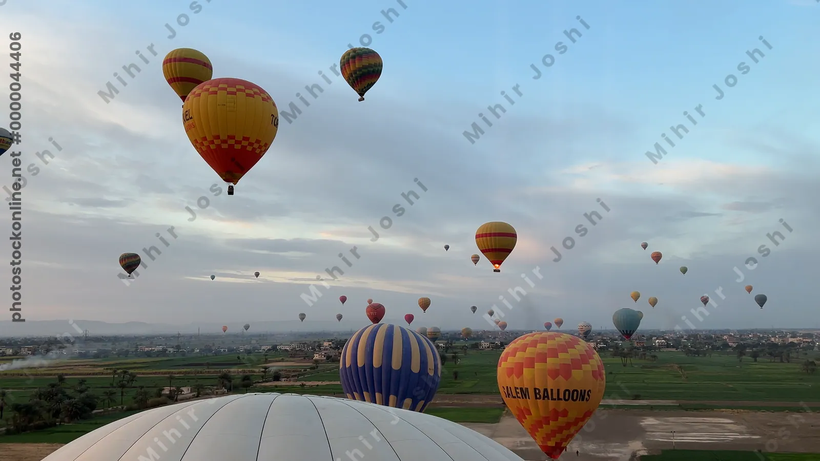 Luxor, Egypt - Feb 10, 2025: Colorful hot air balloons drifting above lush green fields at sunrise, offering a scenic aerial view of the landscape.