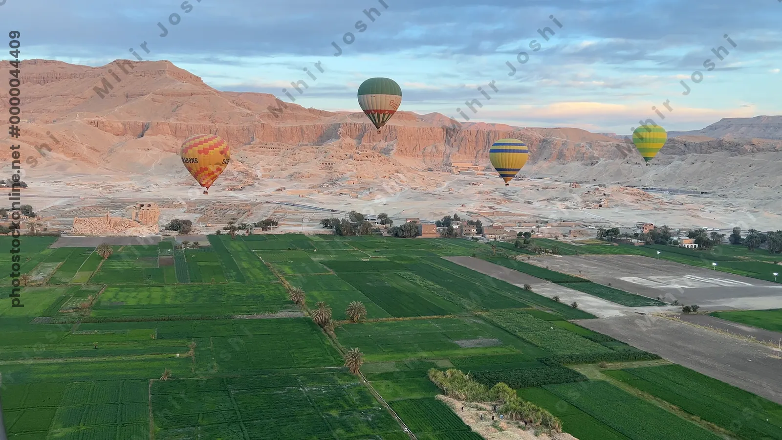 Luxor, Egypt - Feb 10, 2025: Hot air balloons at sunrise floating above green fields and cliffs of Luxor, Egypt, with the Theban mountains in the background.