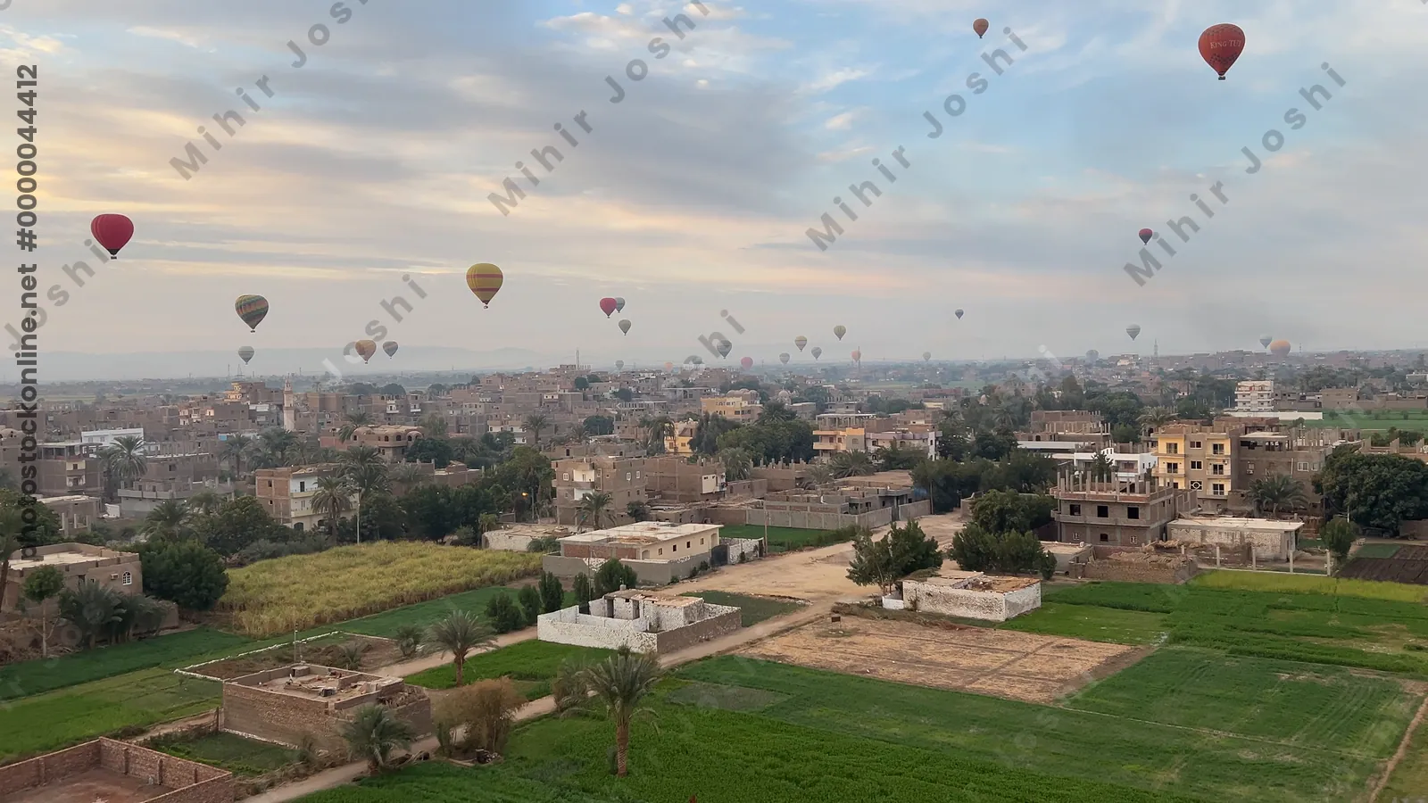 Luxor, Egypt - Feb 10, 2025: Colorful hot air balloons drifting above lush green fields at sunrise, offering a scenic aerial view of the landscape.