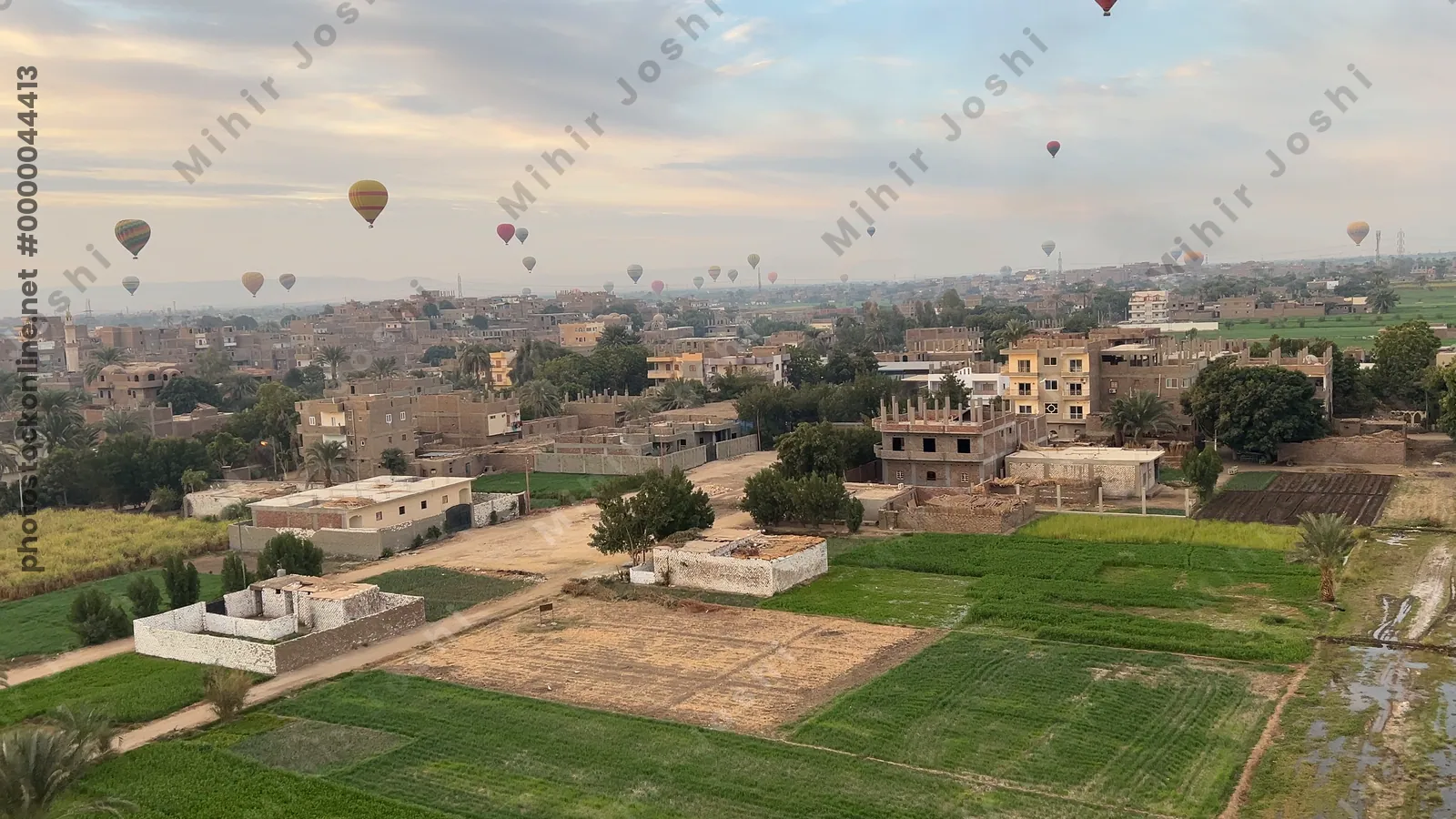 Luxor, Egypt - Feb 10, 2025: Colorful hot air balloons drifting above lush green fields at sunrise, offering a scenic aerial view of the landscape.