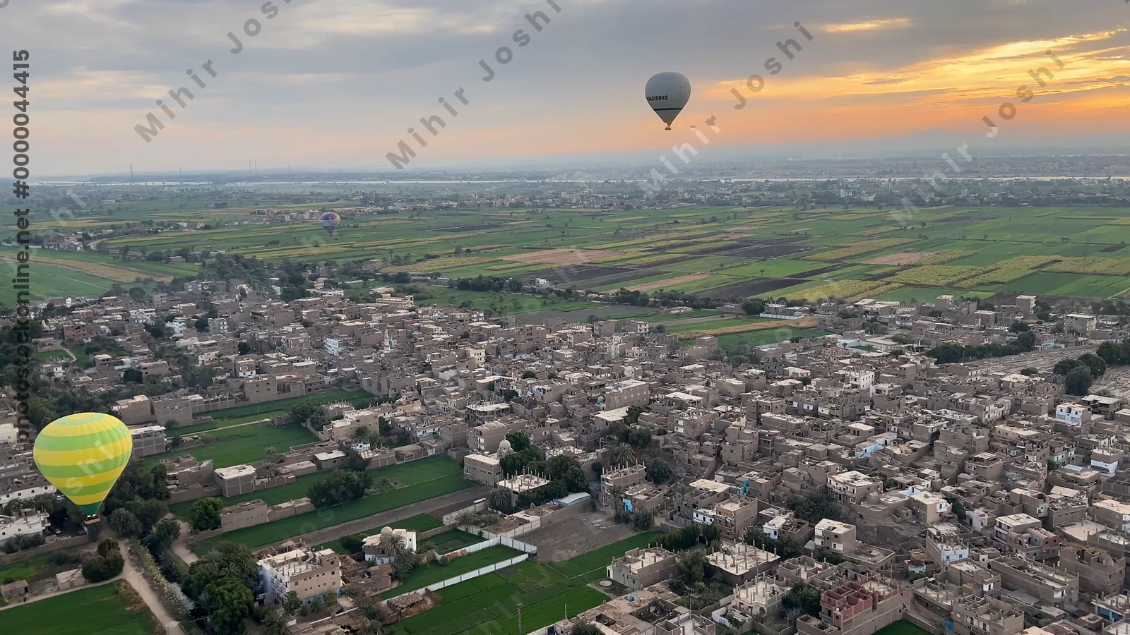 Luxor, Egypt - Feb 10, 2025: Colorful hot air balloons drifting above lush green fields at sunrise, offering a scenic aerial view of the landscape.