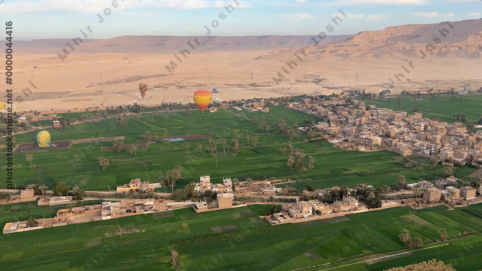 Luxor, Egypt - Feb 10, 2025: Hot air balloons at sunrise floating above green fields and cliffs of Luxor, Egypt, with the Theban mountains in the background.