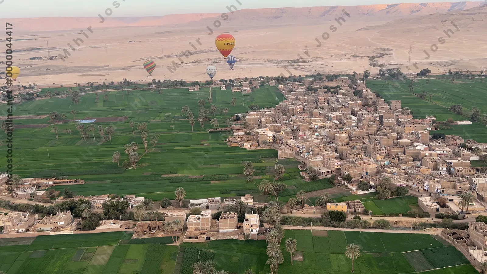 Luxor, Egypt - Feb 10, 2025: Hot air balloons at sunrise floating above green fields and cliffs of Luxor, Egypt, with the Theban mountains in the background.