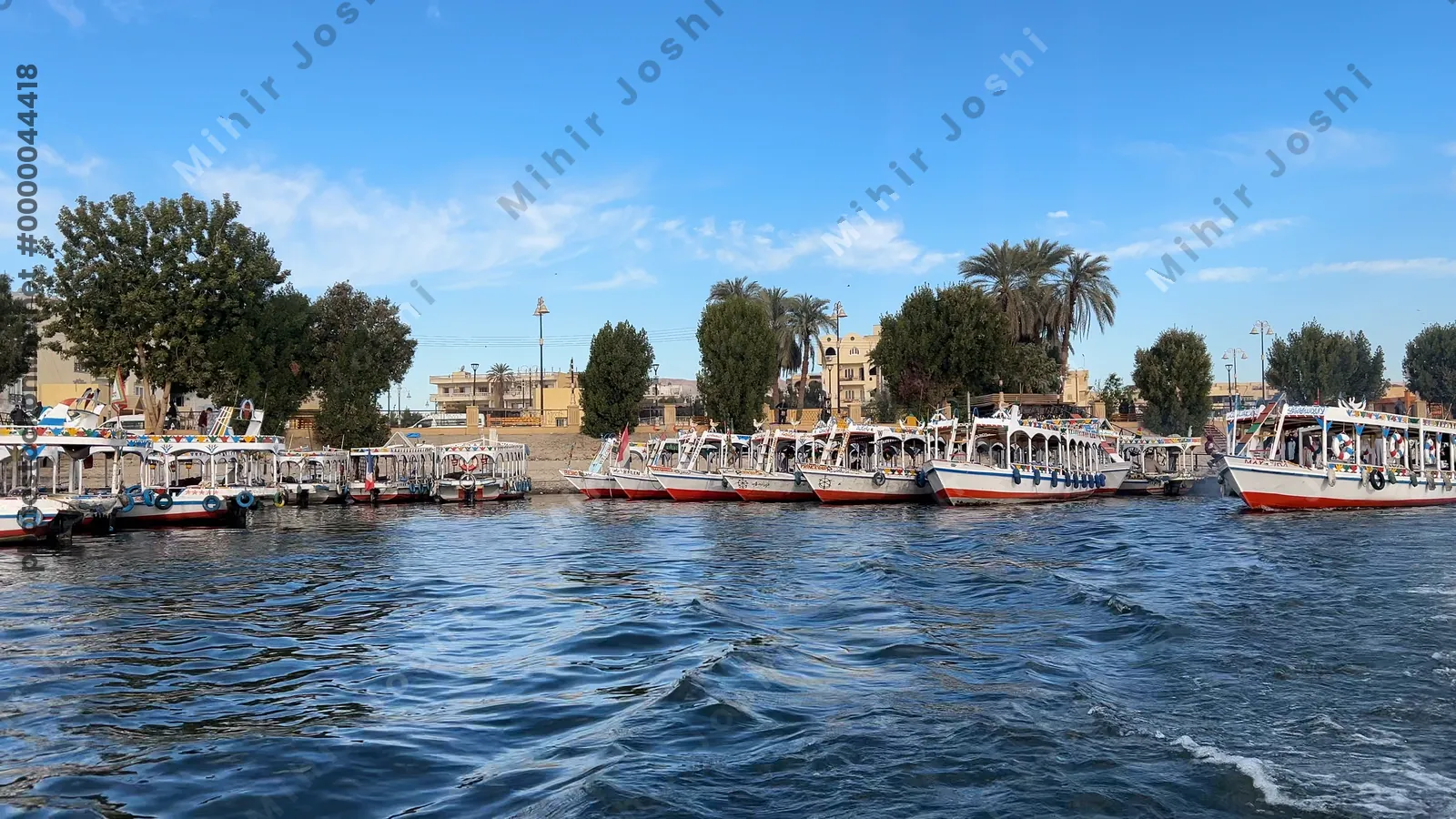 Luxor, Egypt - Feb 10, 2025: Footage of colorful tourist boats docked along the Nile River in Luxor, Egypt, with palm trees and buildings in the background.