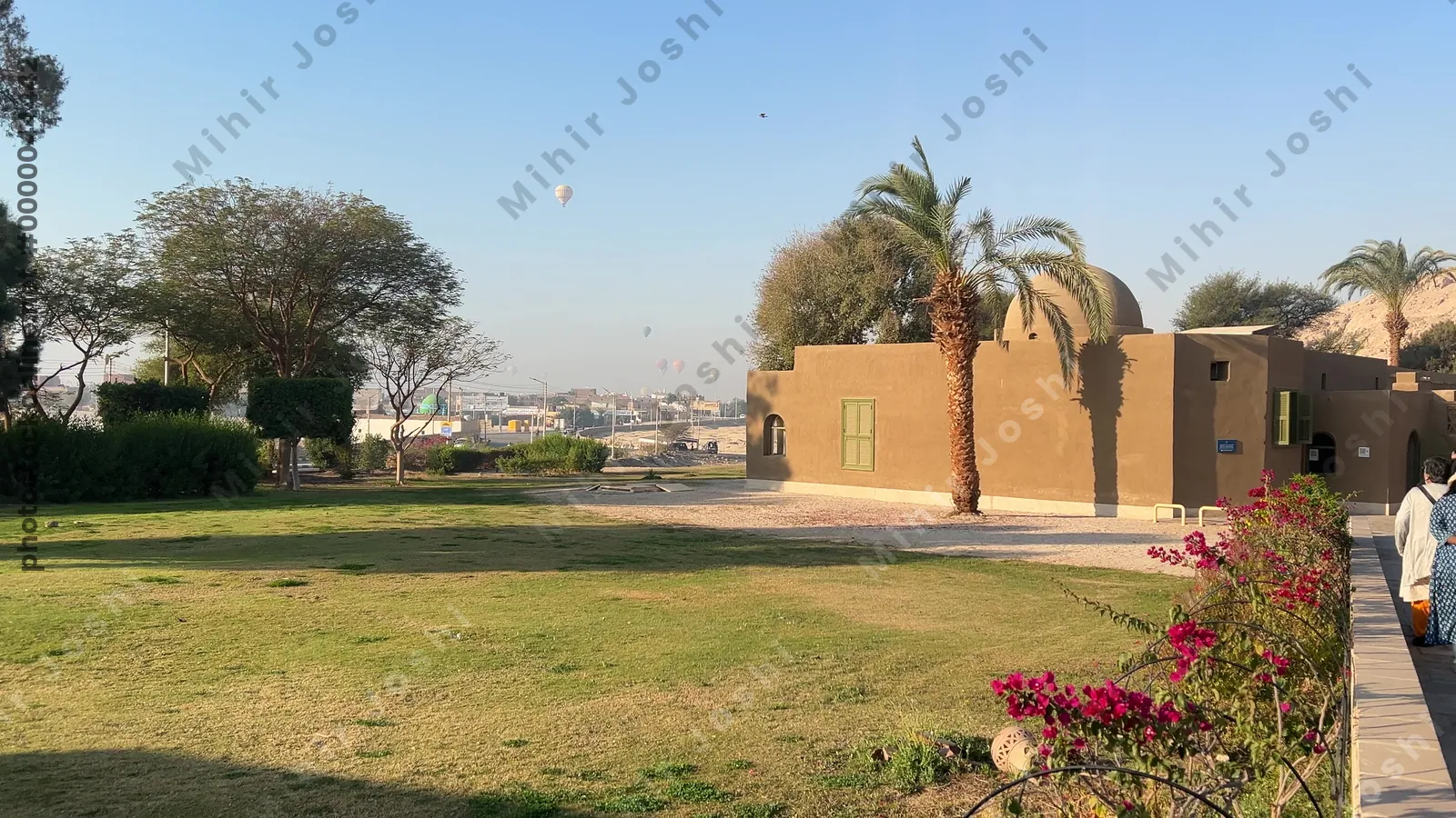 Luxor, Egypt - Feb 11, 2025: Historic Carter House with tourists outside and hot air balloons in the morning sky above Luxor.