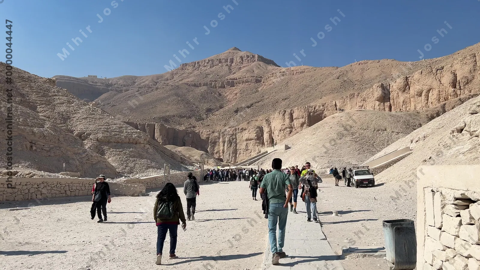Luxor, Egypt - Feb 11, 2025: Visitors walking on a desert path toward tomb entrances at the Valley of the Kings, with cliffs in the background.