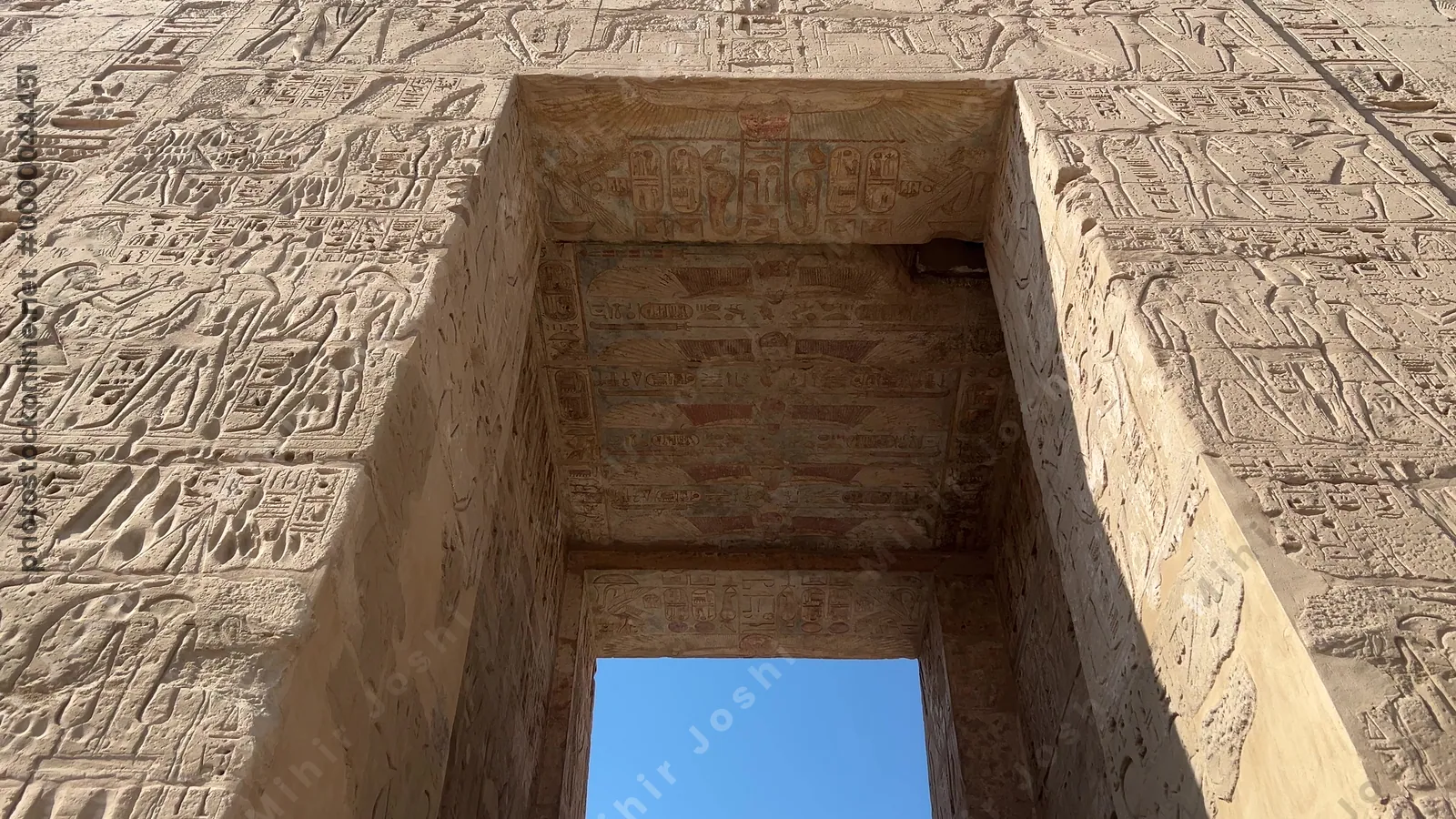 Luxor, Egypt - Feb 11, 2025: Tourists walking through the first pylon of the Mortuary Temple of Ramesses III at Medinet Habu, featuring ancient relief carvings.