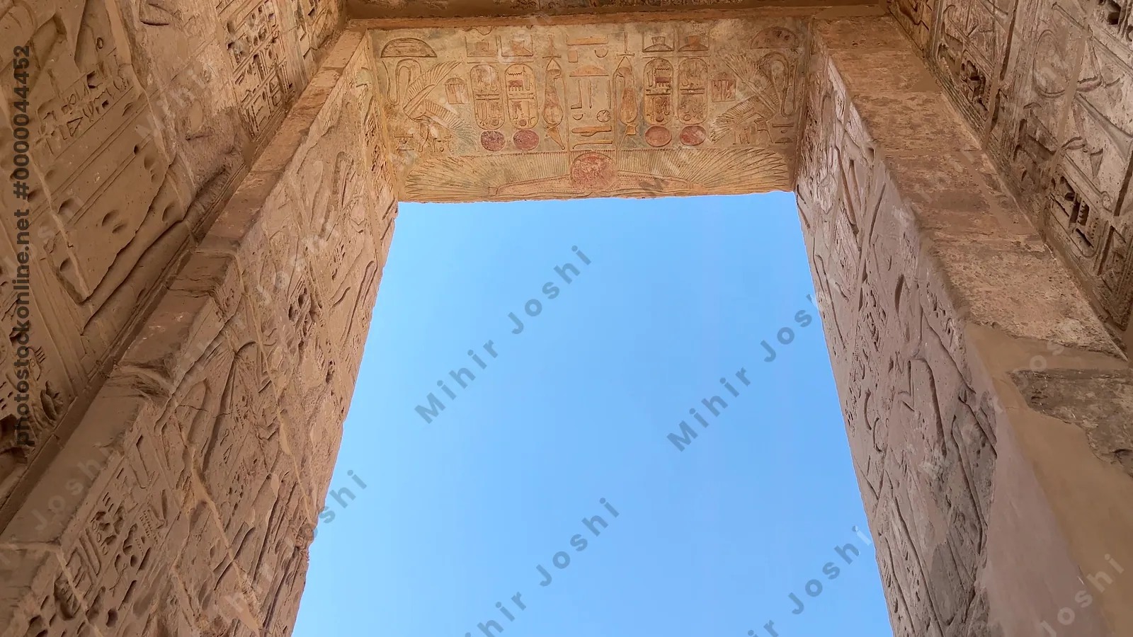 Luxor, Egypt - Feb 11, 2025: Tourists walking through the first pylon of the Mortuary Temple of Ramesses III at Medinet Habu, featuring ancient relief carvings.