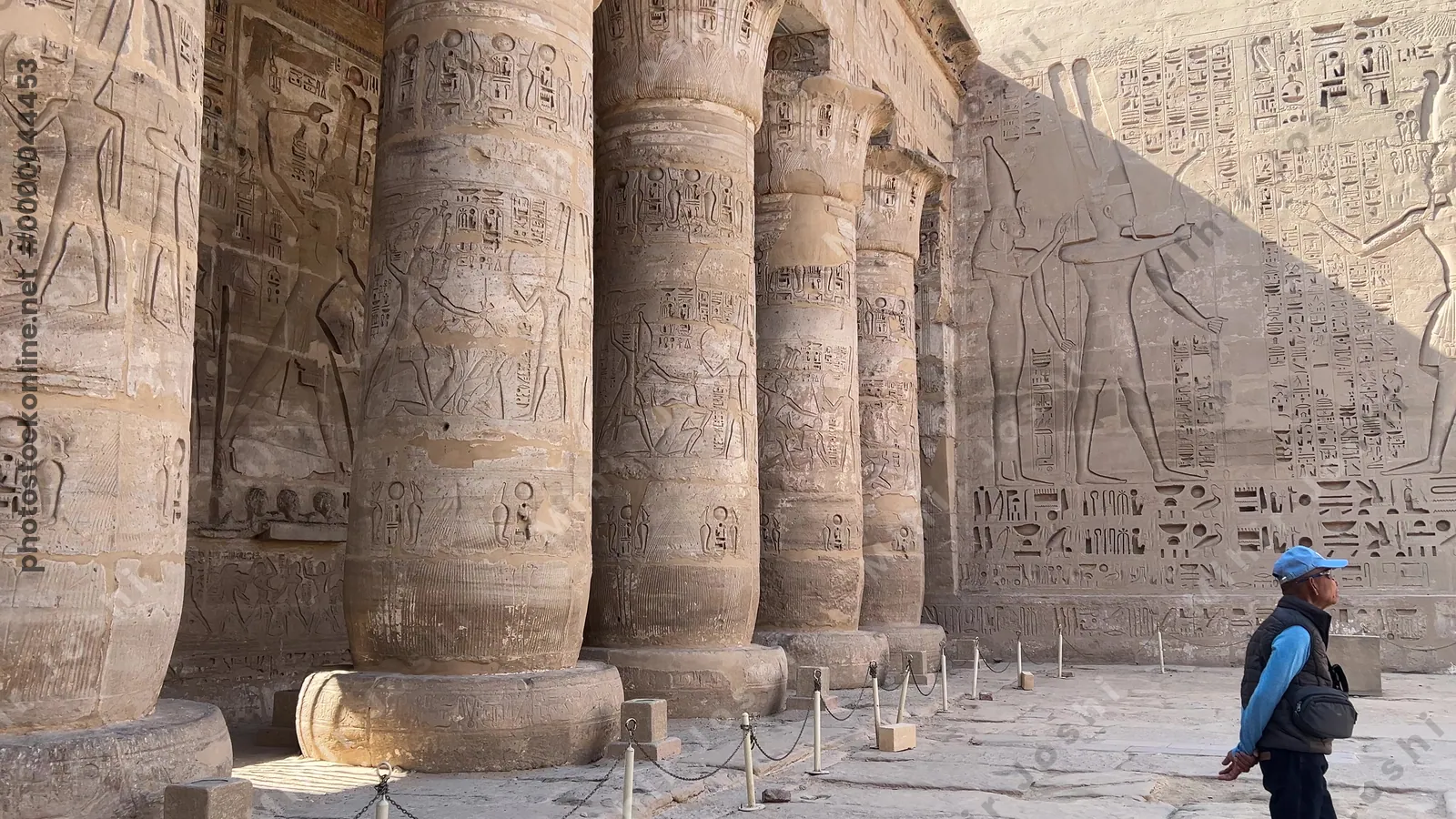 Luxor, Egypt - Feb 11, 2025: Tourists in the courtyard of the Mortuary Temple of Ramesses III at Medinet Habu, showing Osirid statues and papyrus-crowned columns with carved reliefs.
