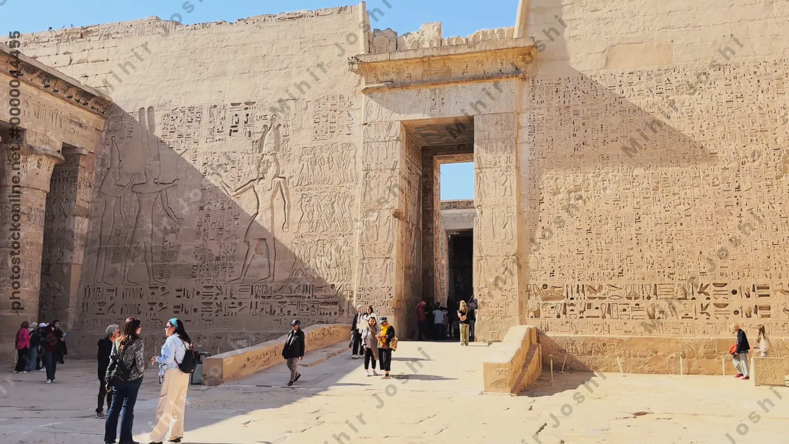 Luxor, Egypt - Feb 11, 2025: Tourists in the courtyard of the Mortuary Temple of Ramesses III at Medinet Habu, showing Osirid statues and papyrus-crowned columns with carved reliefs.